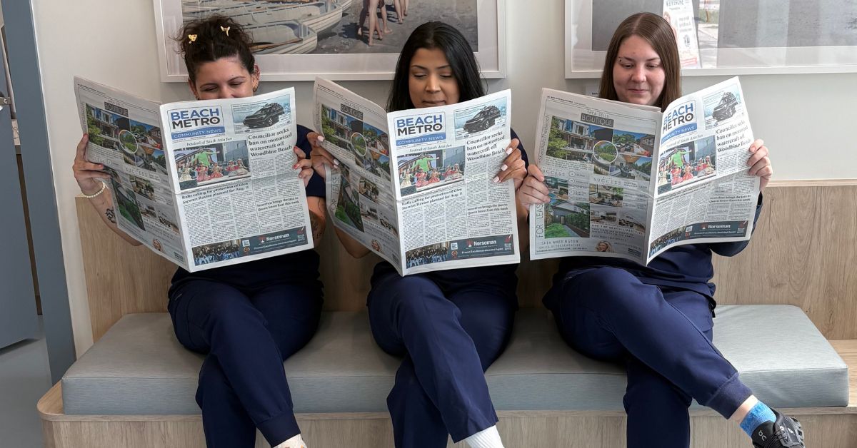 3 women sitting on a bench reading Beach Metro magazine.